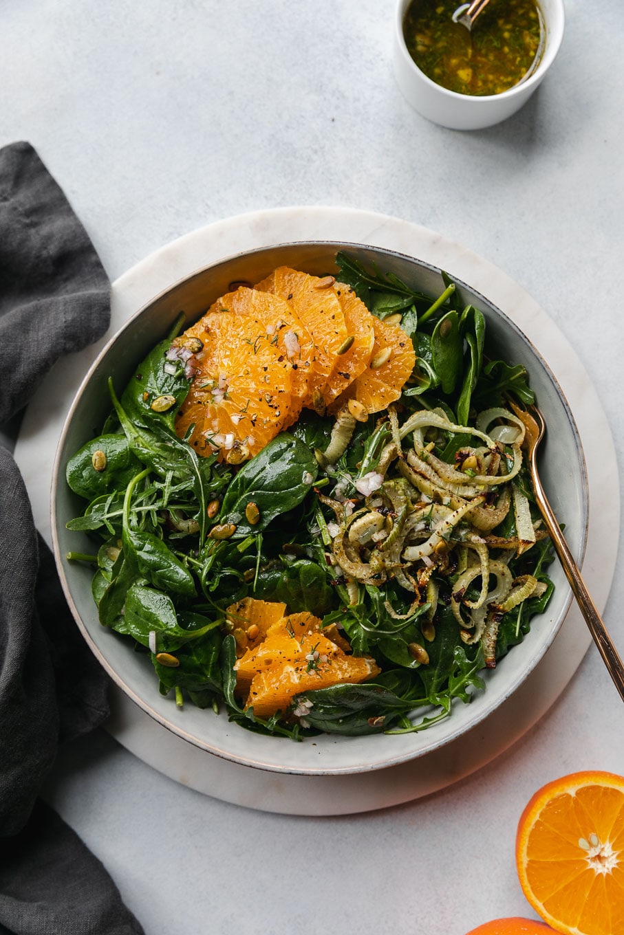 Overhead shot of a spinach arugula salad with roasted fennel, tangelos, and toasted pumpkin seeds with a gold fork in the bowl