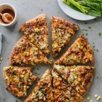 Overhead shot of a pizza cut into slices with a bite taken out of the slice in the bottom left corner