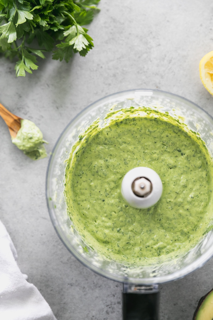 Overhead shot of a food processor filled with creamy green dressing and a wooden spoon with dressing on it off to the side