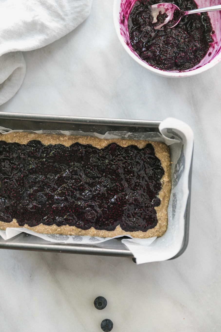 Overhead shot of a loaf pan filled with banana bread batter and a layer of blueberry chia jam