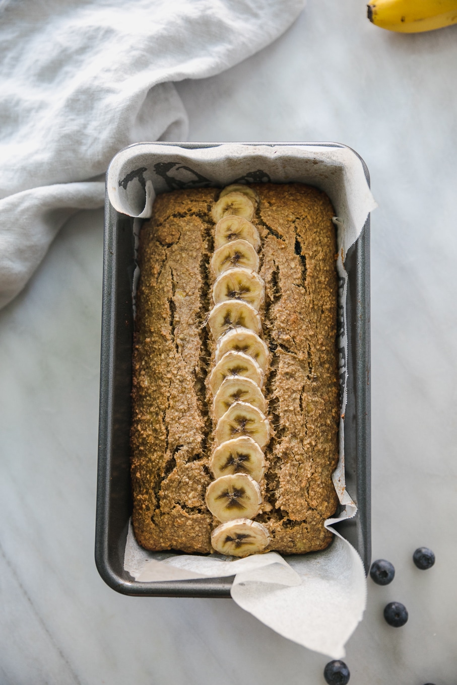 Overhead shot of a loaf of banana bread in a loaf pan with a row of sliced banana on top
