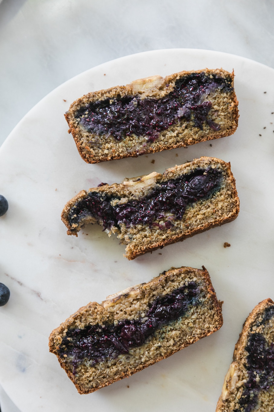 Overhead close up shot of slices of blueberry chia jam stuffed banana bread with a bite taken out of one of the slices