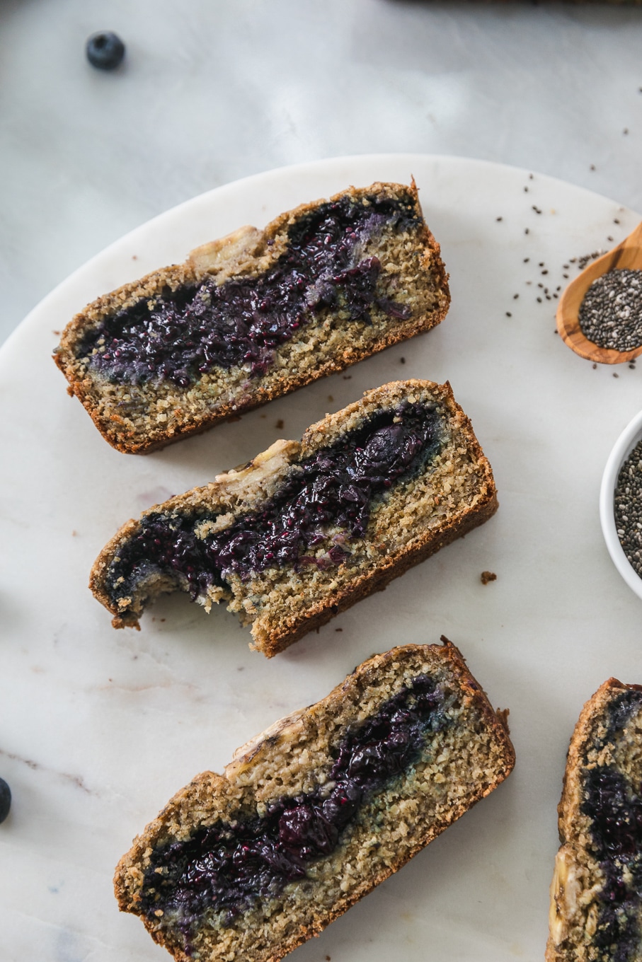 Overhead close up shot of slices of blueberry chia jam stuffed banana bread with a bite taken out of one of the slices
