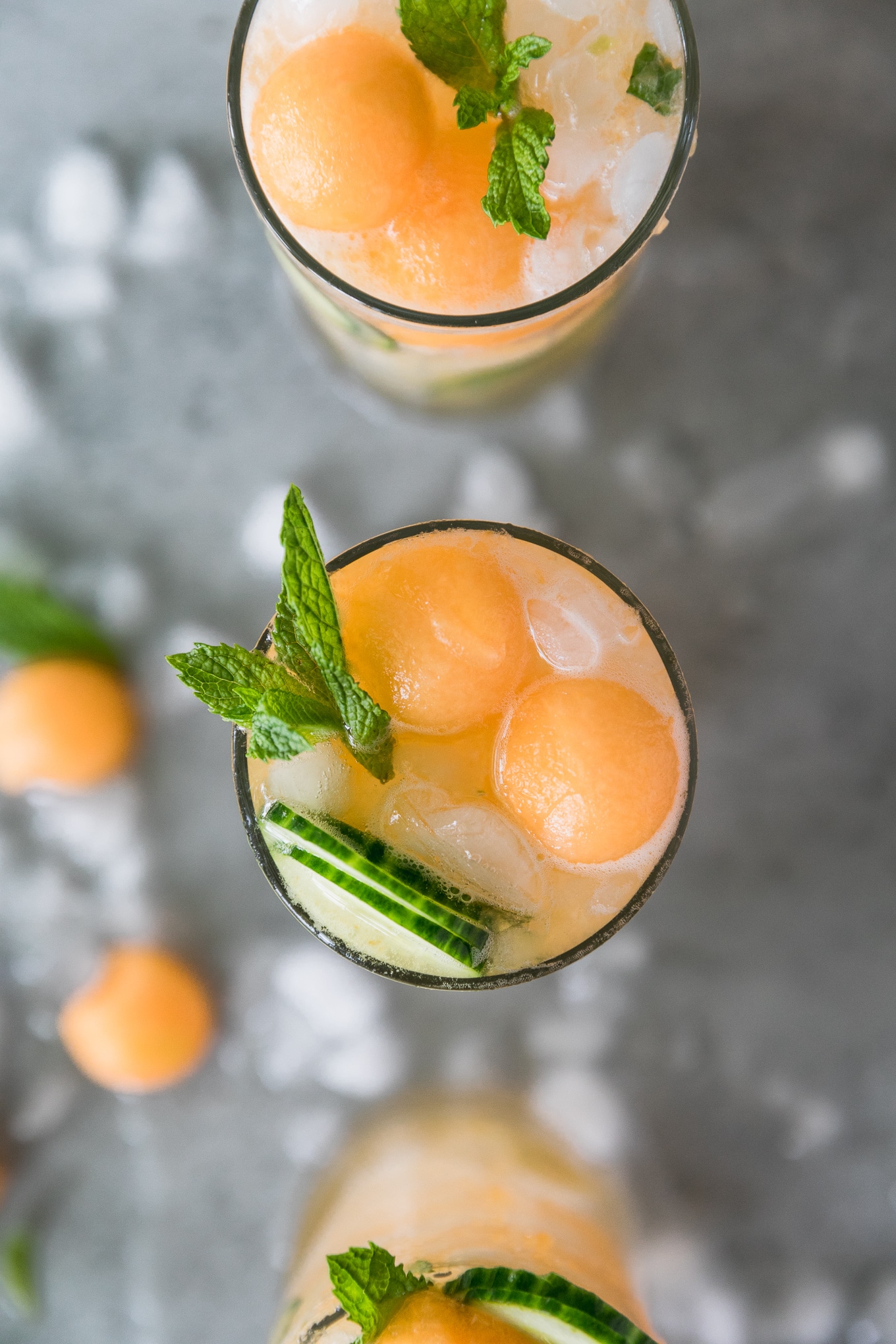 Overhead shot of three cocktails topped with melon balls, sliced cucumber, and a spring of mint
