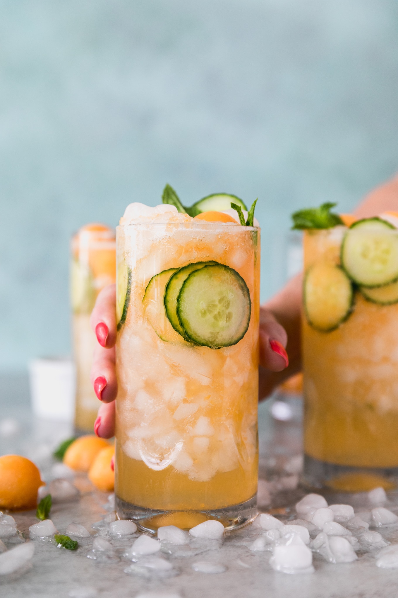 Forward facing shot of 3 cucumber melon cocktails with a hand reaching out and holding the closest one