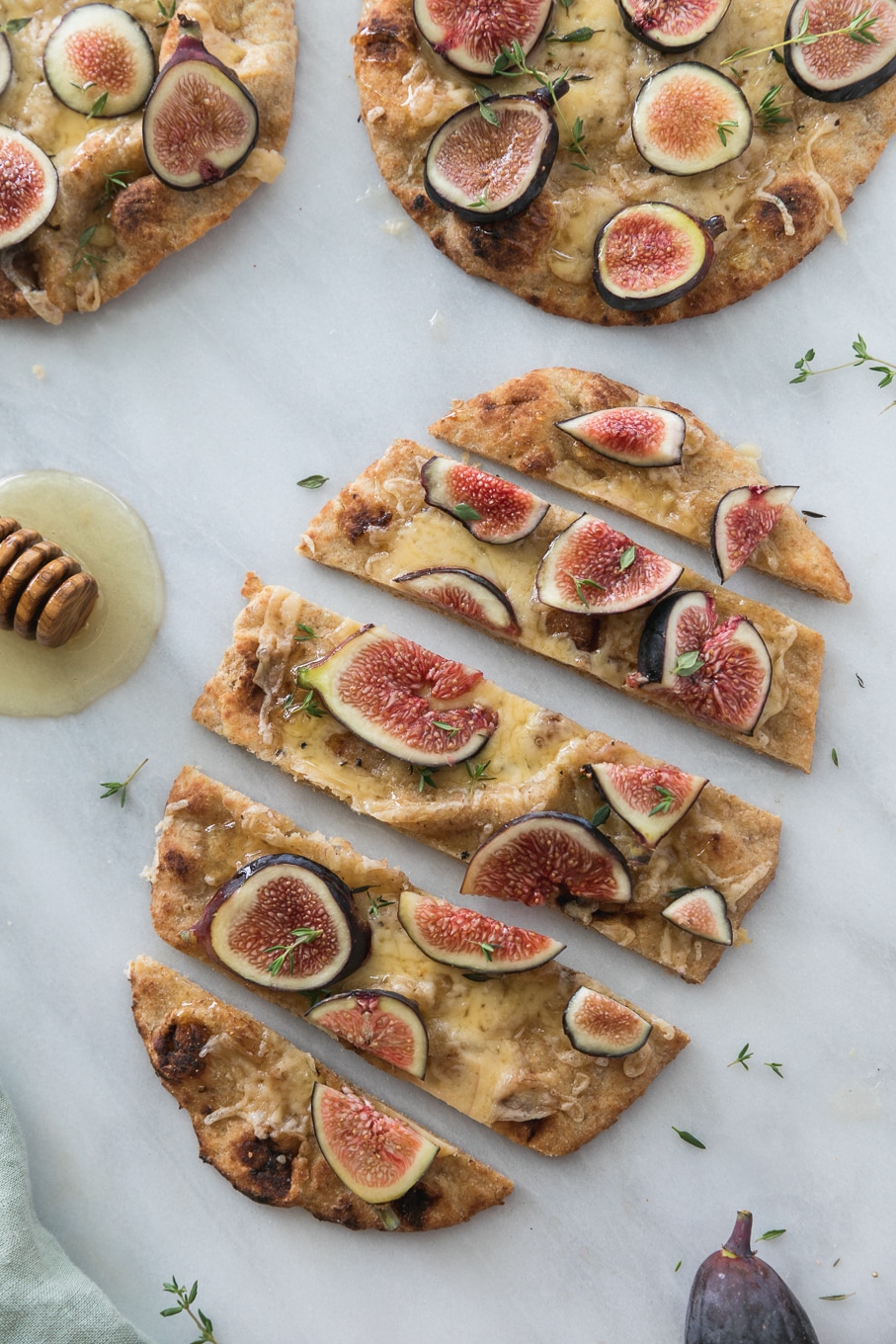 Overhead shot of a fig flatbread sliced into pieces and a honey dipper next to it