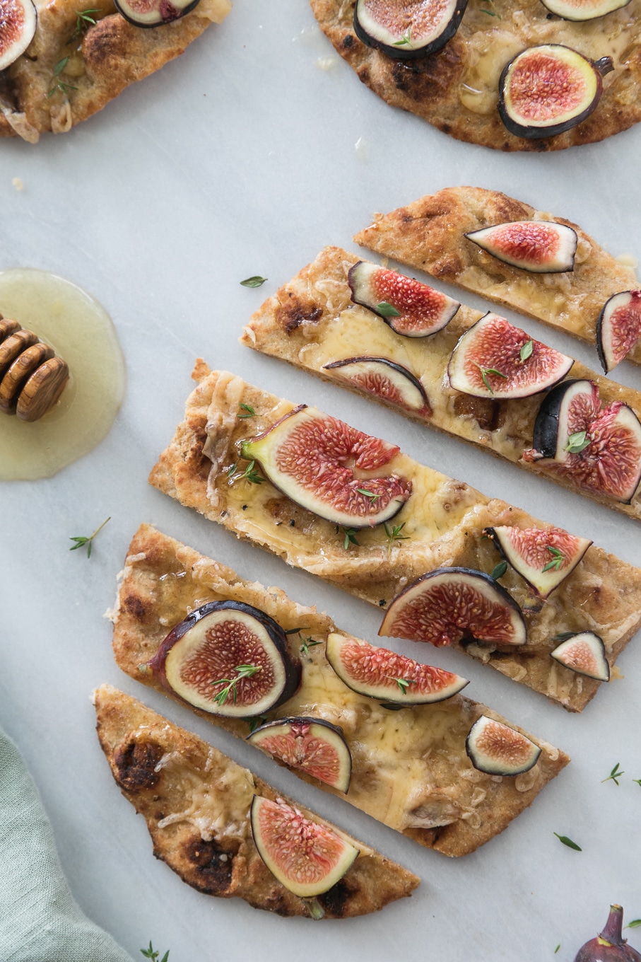 Overhead close up shot of a fig flatbread sliced into pieces and a honey dipper next to it