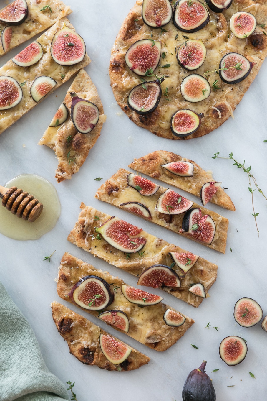 Overhead shot of 3 fig flatbreads sliced into pieces with thyme sprigs and a honey dipper alongside them