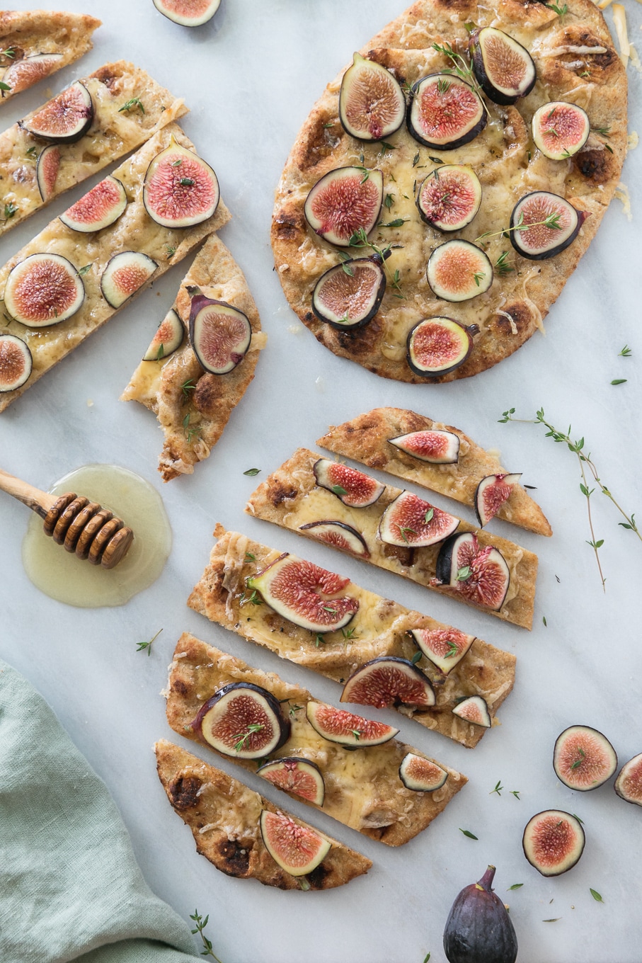 Overhead shot of 3 fig flatbreads sliced into pieces with thyme sprigs and a honey dipper alongside them