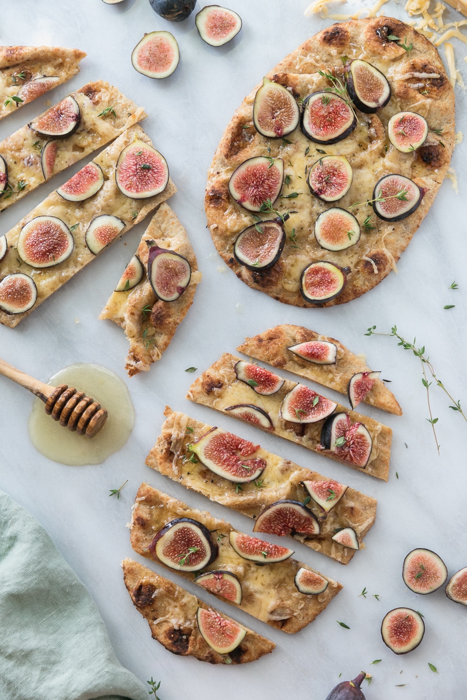 Overhead shot of 3 fig flatbreads sliced into pieces with thyme sprigs and a honey dipper alongside them