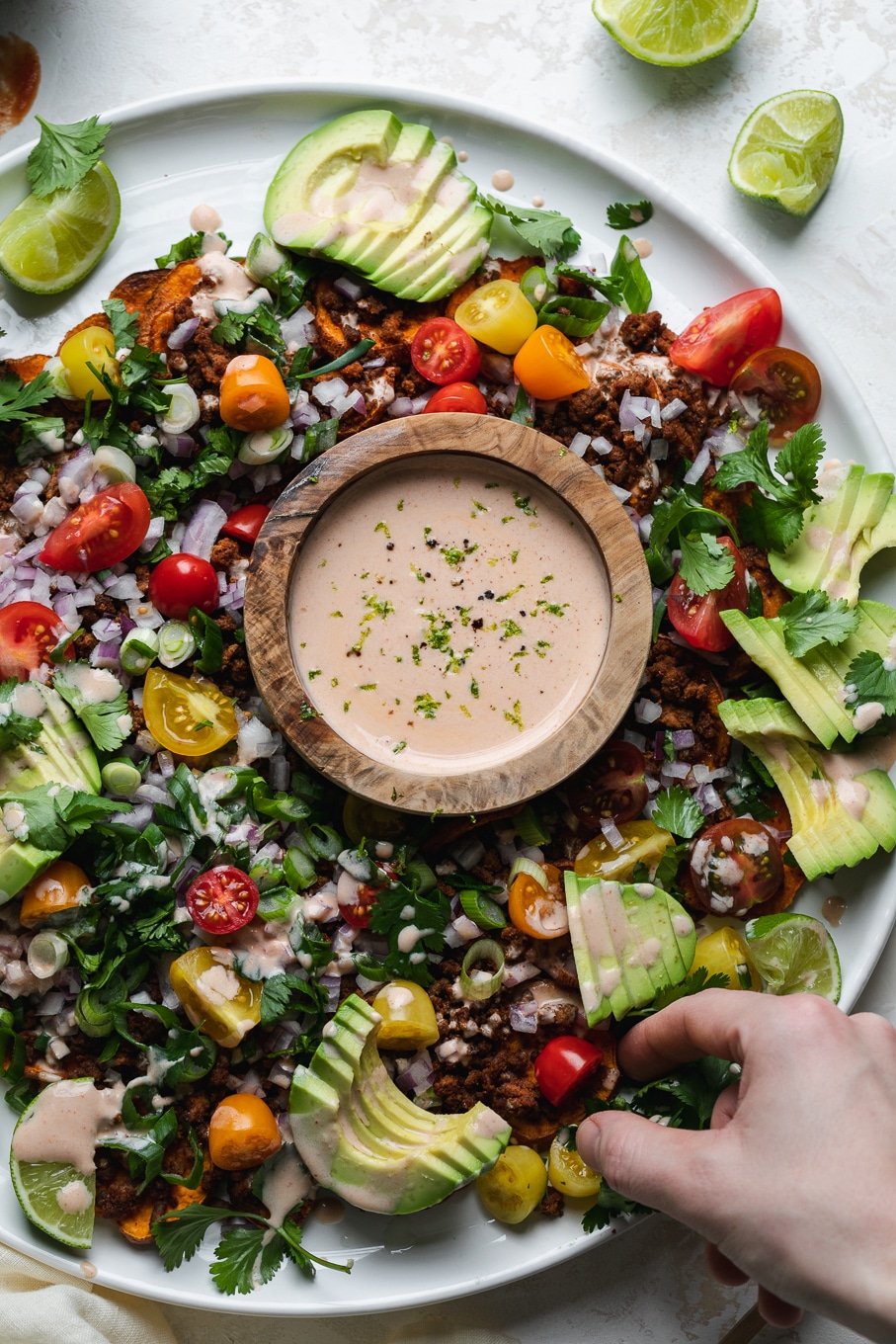 Overhead shot of a plate of nachos with colorful toppings and a hand reaching in
