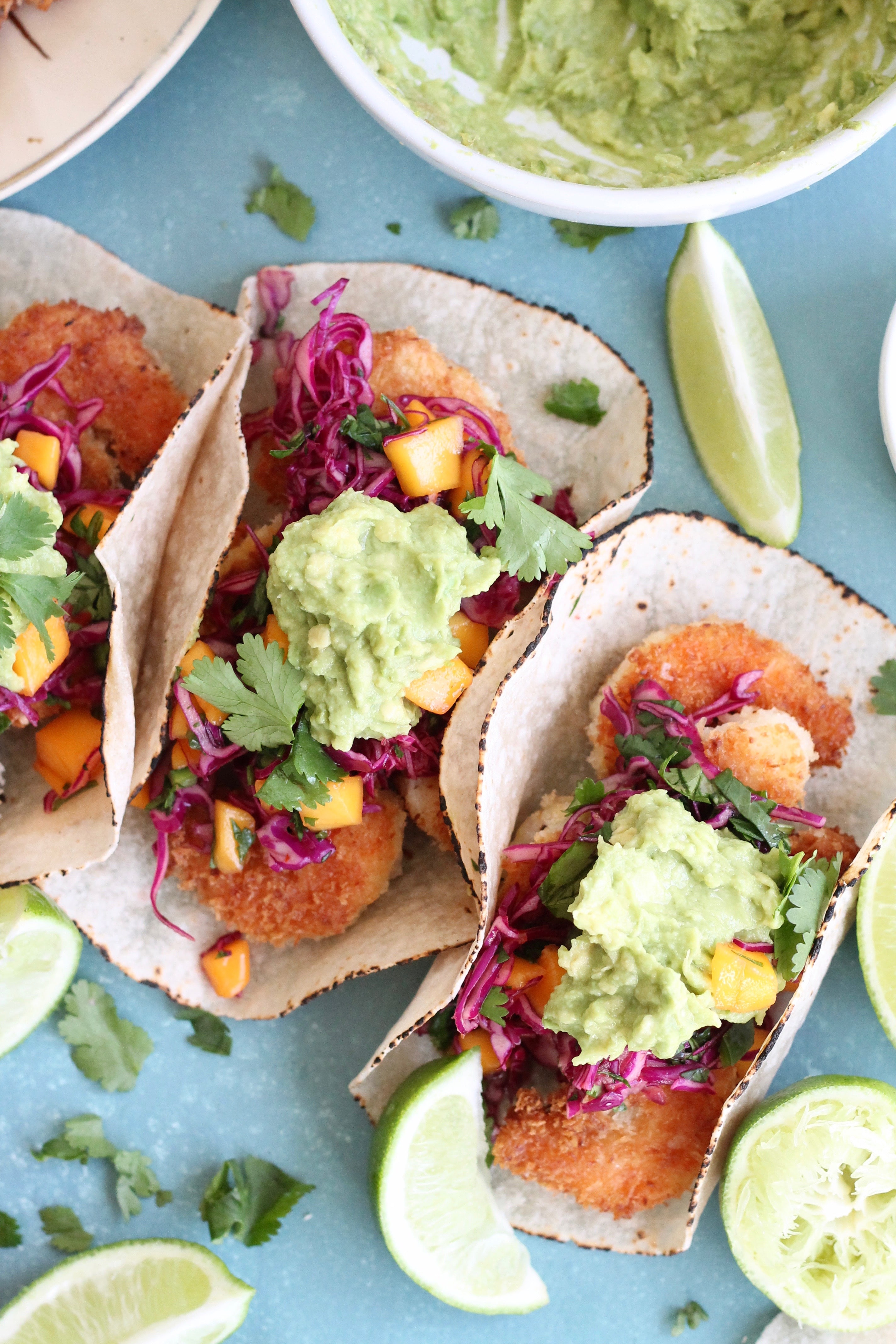 Overhead closeup shot of coconut shrimp tacos topped with mango sweet chili slaw and avocado mash