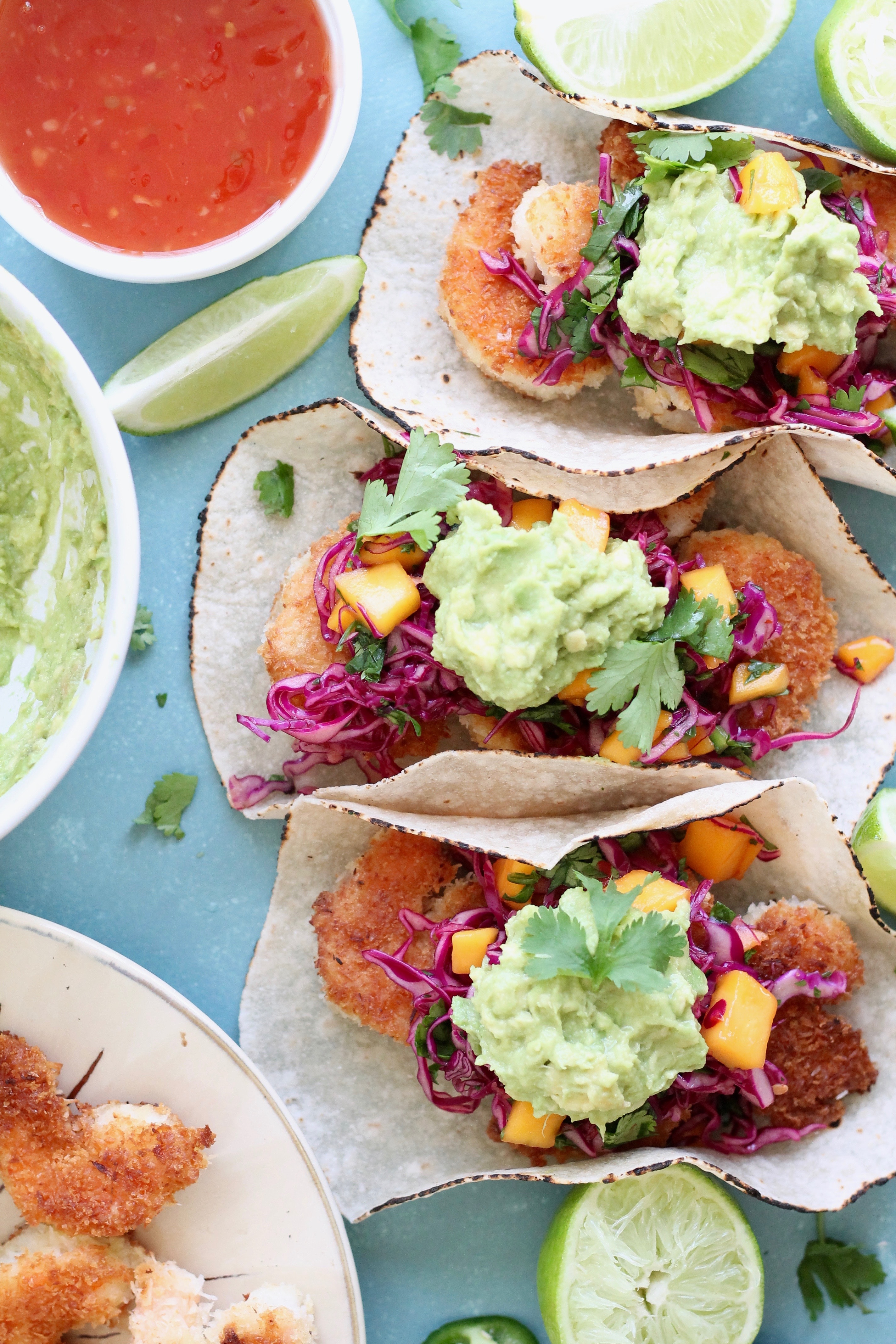 Overhead shot of three coconut shrimp tacos topped with mango sweet chili slaw and avocado mash