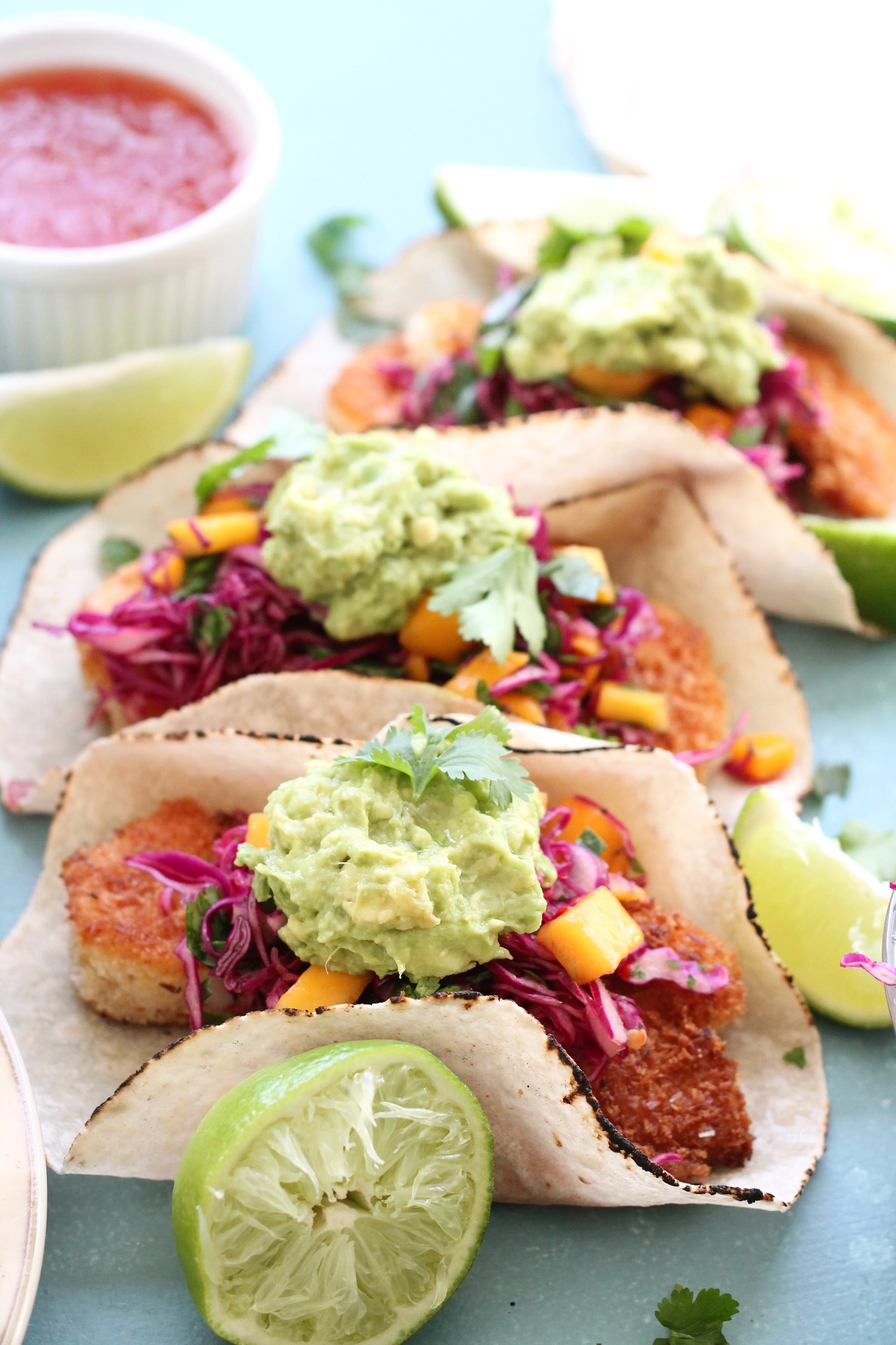 Closeup shot of coconut shrimp tacos with avocado mash, lime, and sweet chili slaw