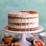 Straight on shot of blood orange layer cake with pink glaze dripping down the sides and candied blood oranges on top