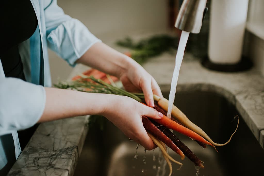 Hands washing rainbow carrots in the sink with running water dripping