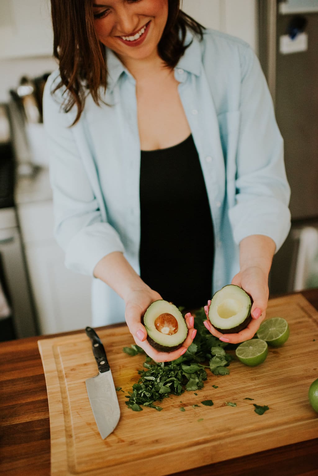 Shot of a woman smiling and holding a halved avocado