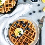 Overhead shot of a waffle with another waffle sticking out in the top left corner and blueberries scattered around