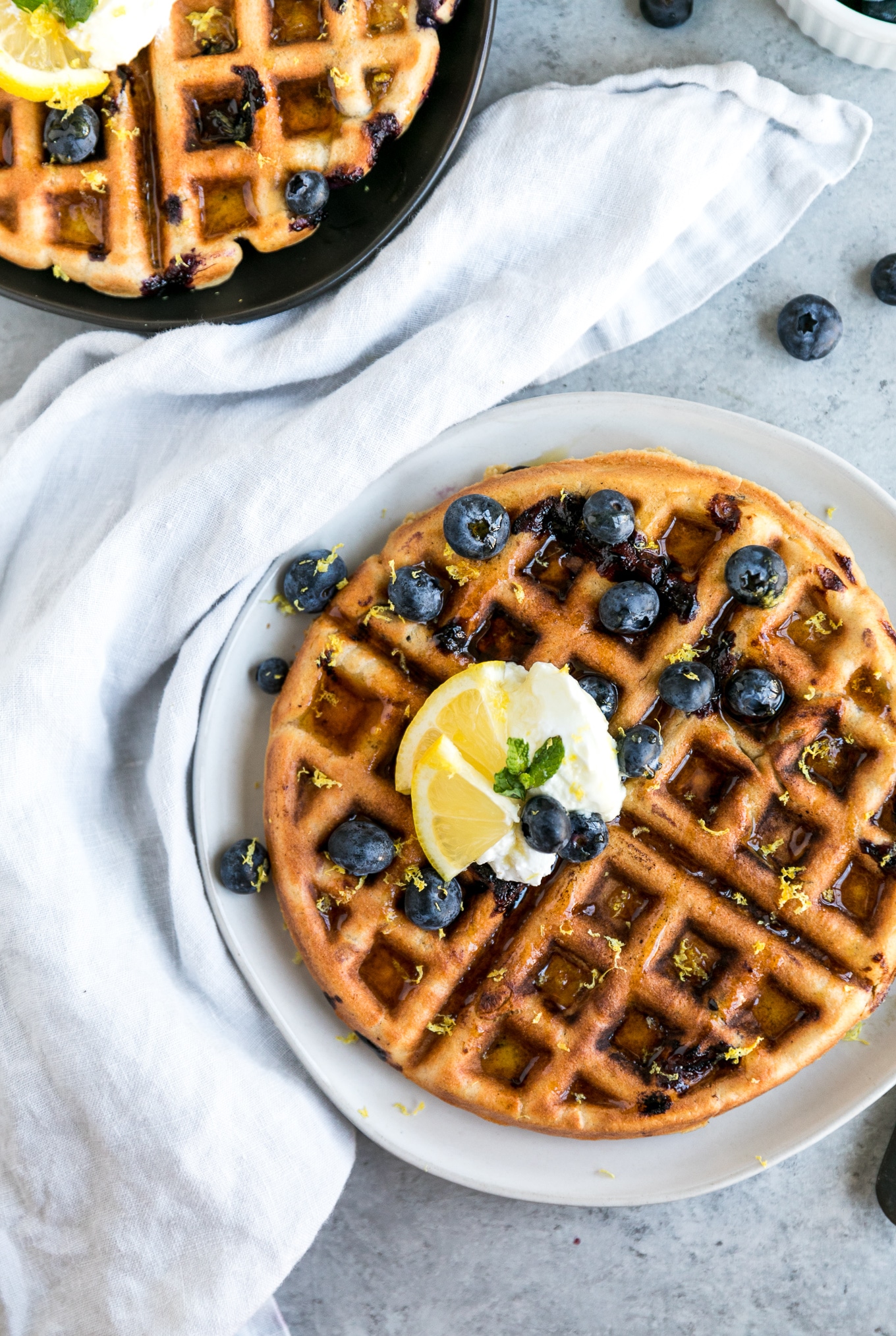 Overhead shot of a waffle topped with blueberries, greek yogurt, and lemon slices