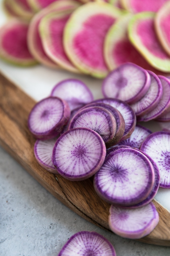 Close up shot of purple daikon radishes and hot pink watermelon radishes on a marble and wood board