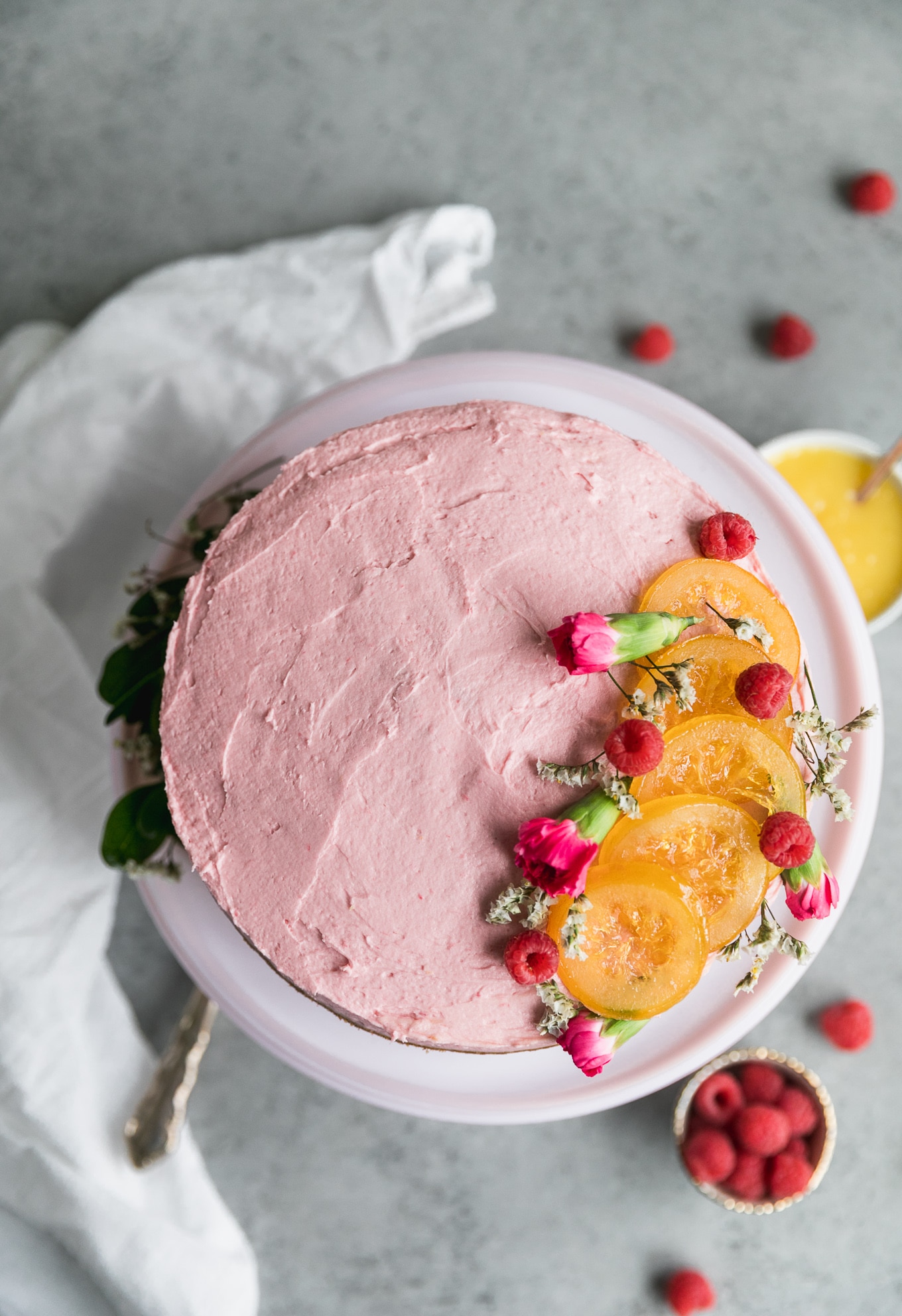 Overhead shot of a pink cake decorated with candied lemon slices, flowers and raspberries