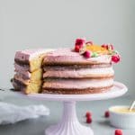 Forward facing shot of a three layer cake iced with pink icing, and a slice being pulled out of the left side of the cake