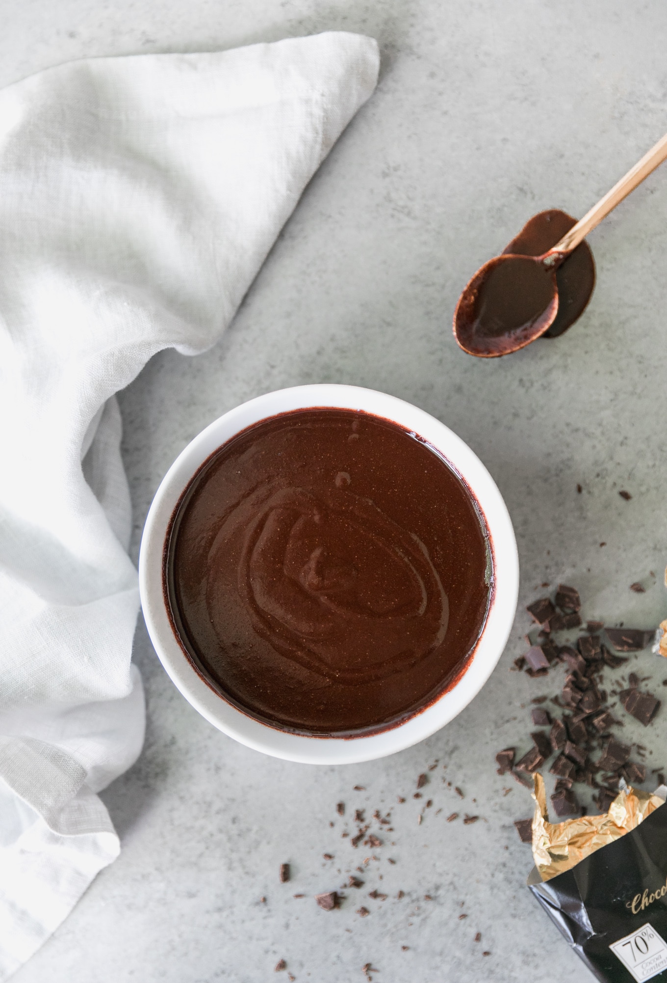 Overhead shot of a bowl of chocolate fudge sauce with a chocolate dipped gold spoon in the top right and chopped chocolate in the bottom right