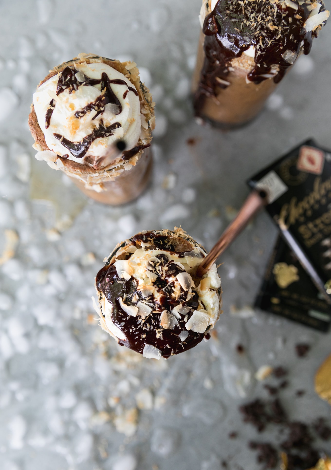 Overhead shot of 2 iced coffees topped with whipped cream, chocolate sauce, and toasted coconut, with two chocolate bars off to the side