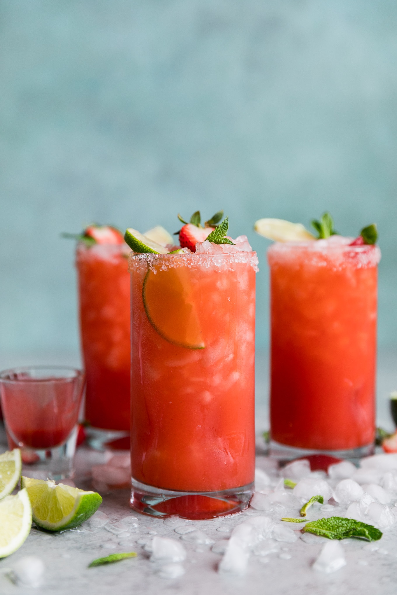 Forward facing shot of three strawberry margaritas with crushed ice on the table and a blue background