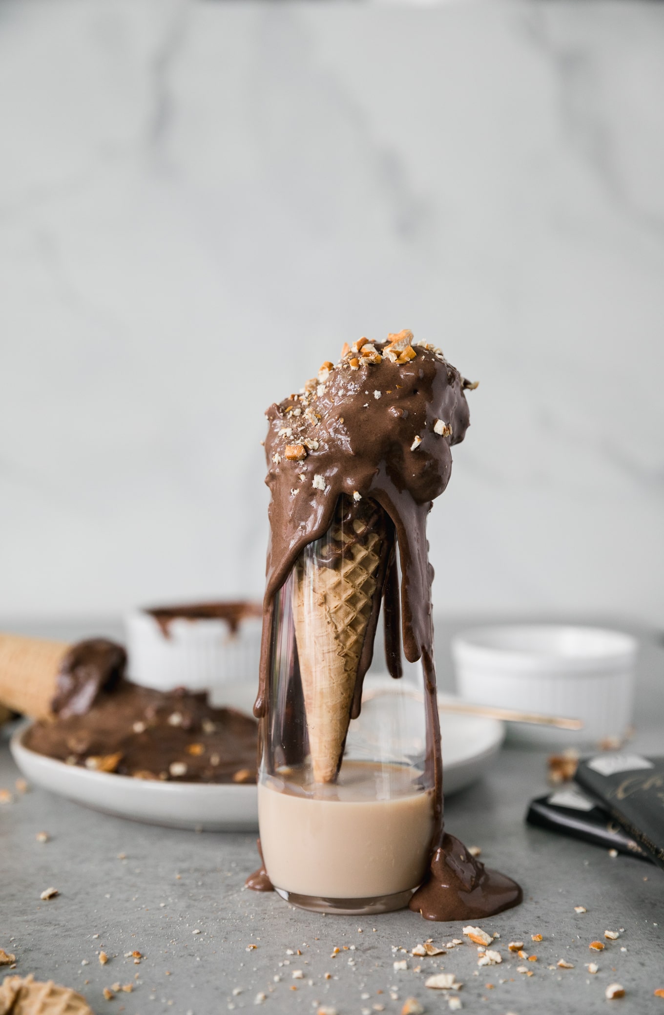 Forward facing shot of a tall skinny glass with Irish cream liquer at the bottom, and a drippy chocolate peanut butter pretzel ice cream cone inside the glass