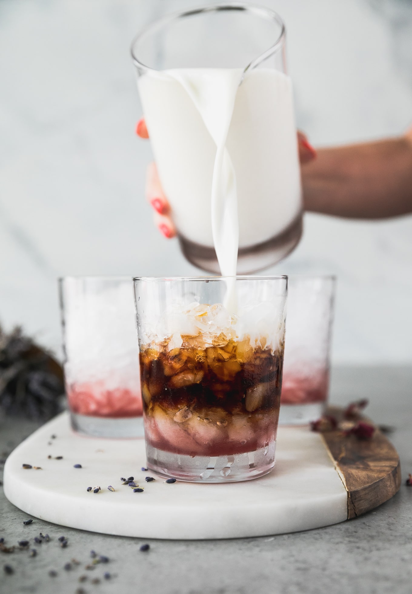 Forward facing shot of a glass filled with pink simple syrup, crushed ice, an espresso shot, and milk being poured into it