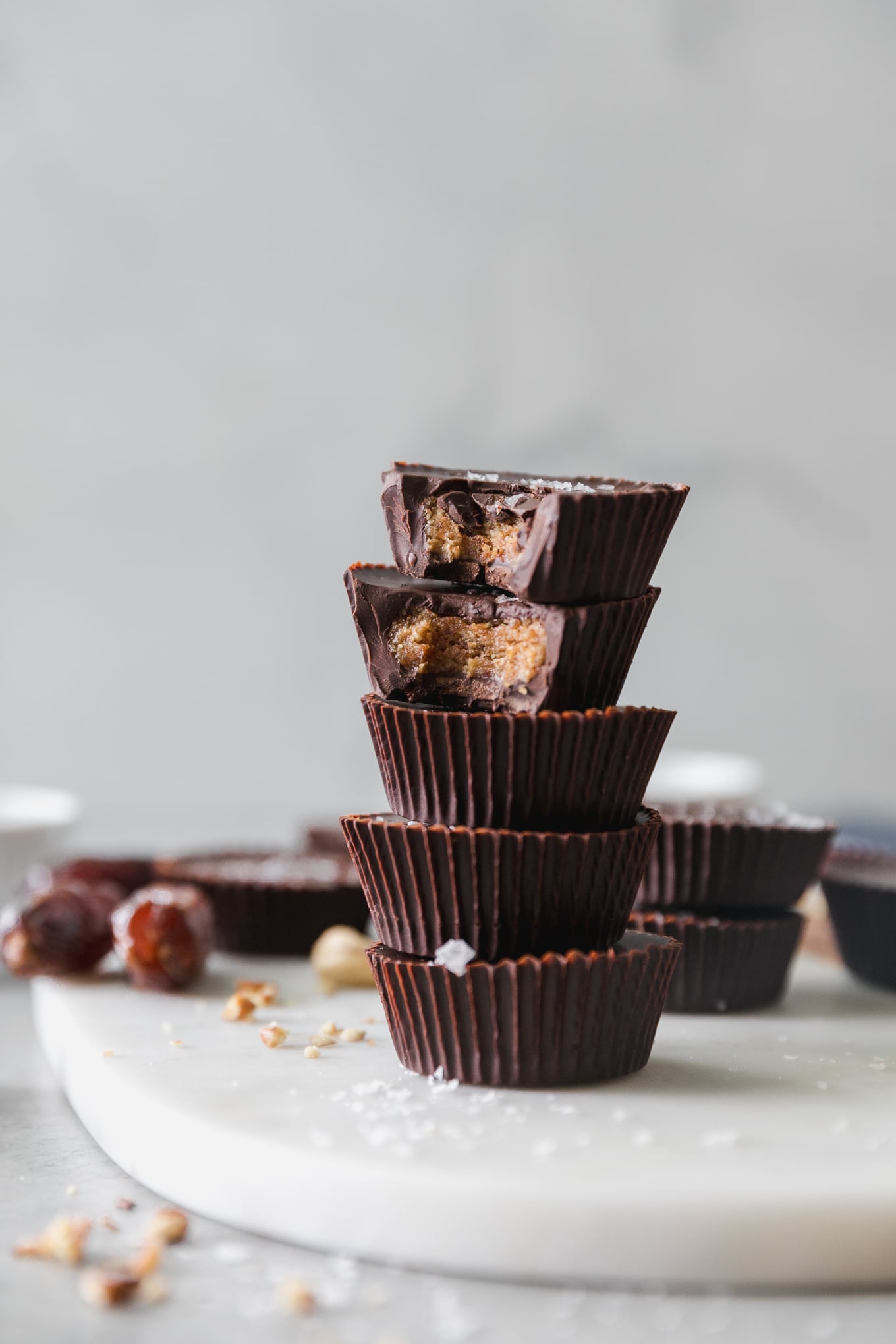 Forward facing stack of 5 peanut butter cups, with bites taken out of the top 2, and more peanut butter cups, dates, and nuts scattered in the background