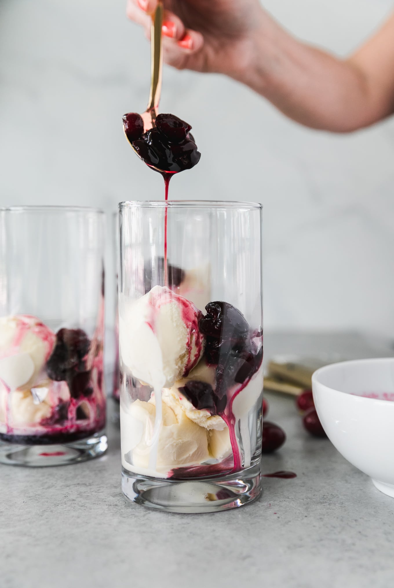 Forward facing shot of a glass filled with scoops of vanilla ice cream and macerated cherries being drizzled into the glass