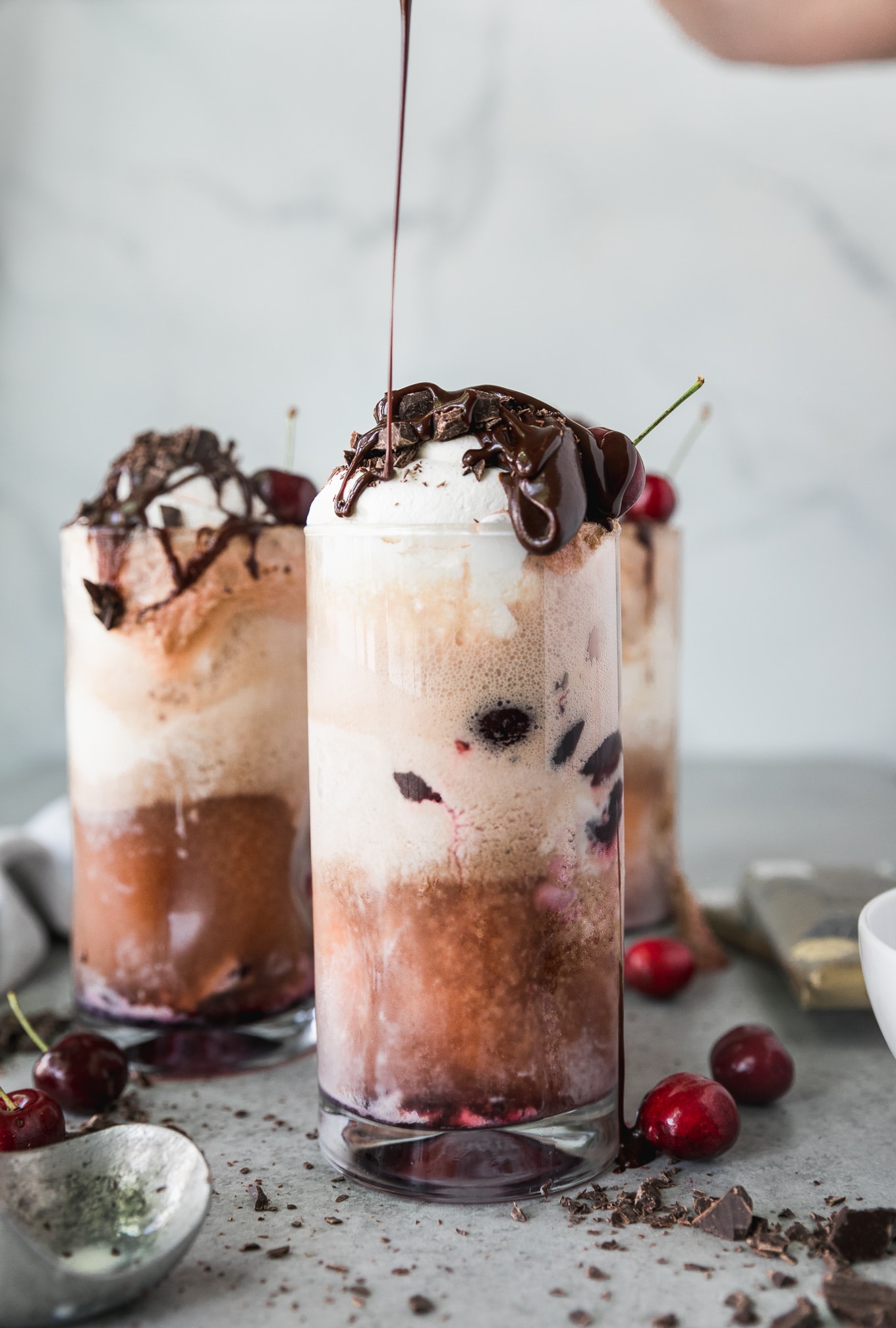 Forward facing shot of a chocolate cherry bourbon float being drizzled with chocolate fudge sauce