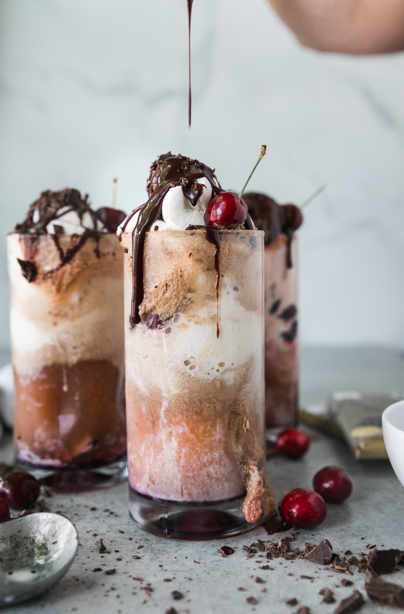 Forward facing shot of a chocolate cherry bourbon float being drizzled with chocolate fudge sauce