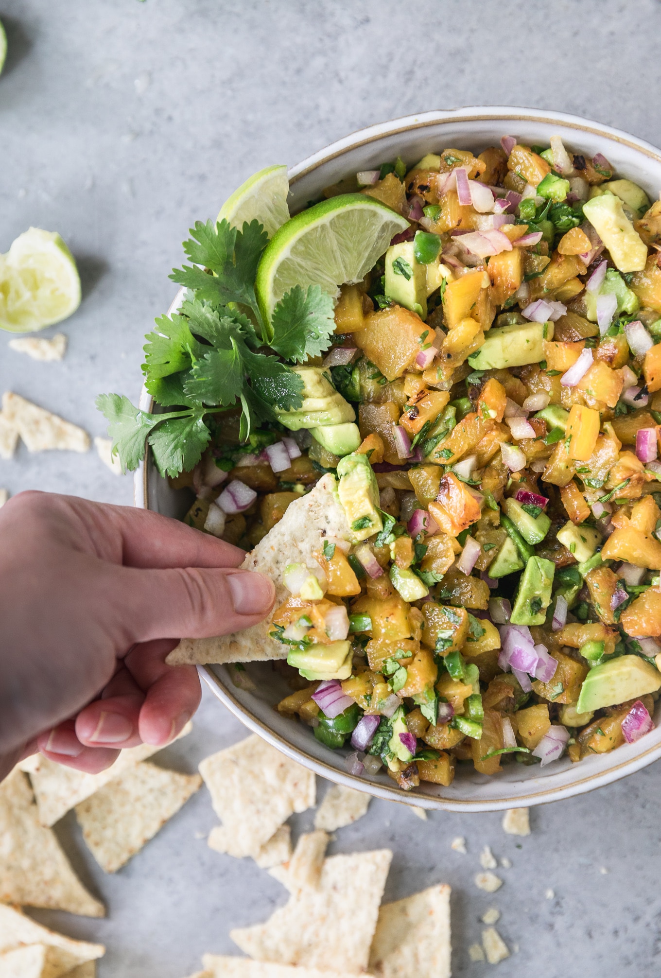 Overhead close up shot of a bowl of grilled pineapple avocado salsa with a hand scooping some out with a chip