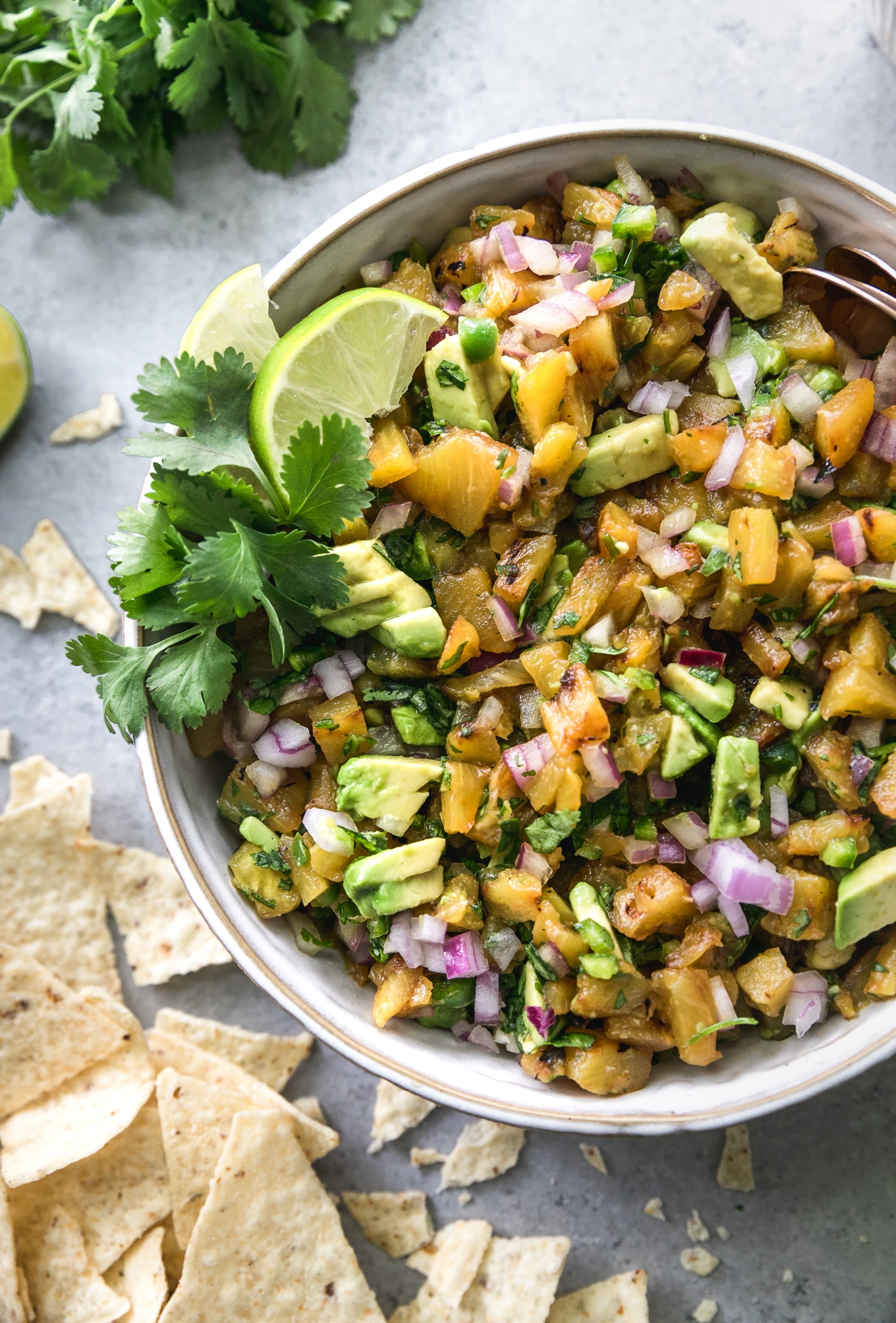 Overhead close up shot of a bowl of grilled pineapple avocado salsa with chips scattered around next to it