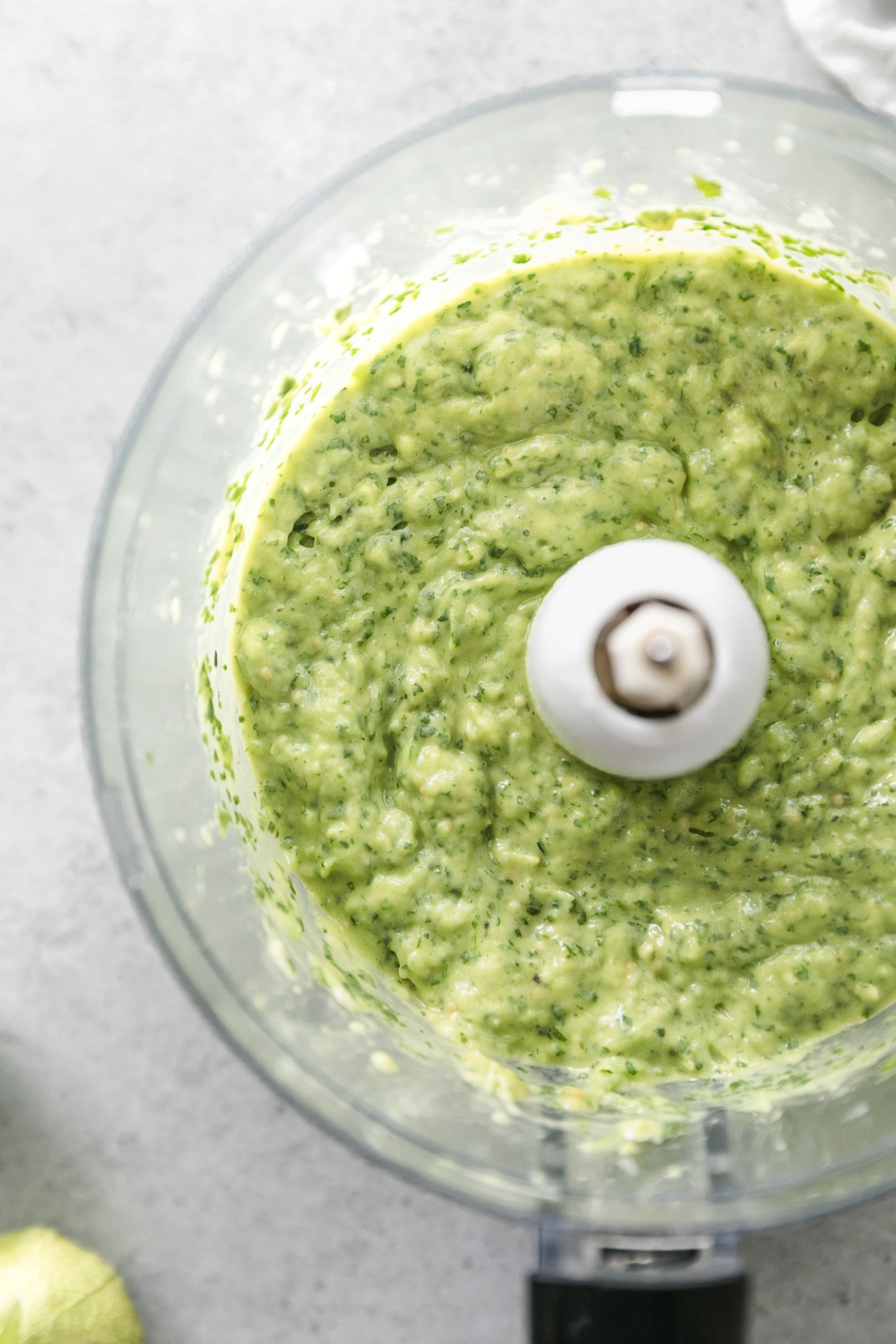 Overhead shot of a food processor filled with green avocado salsa verde