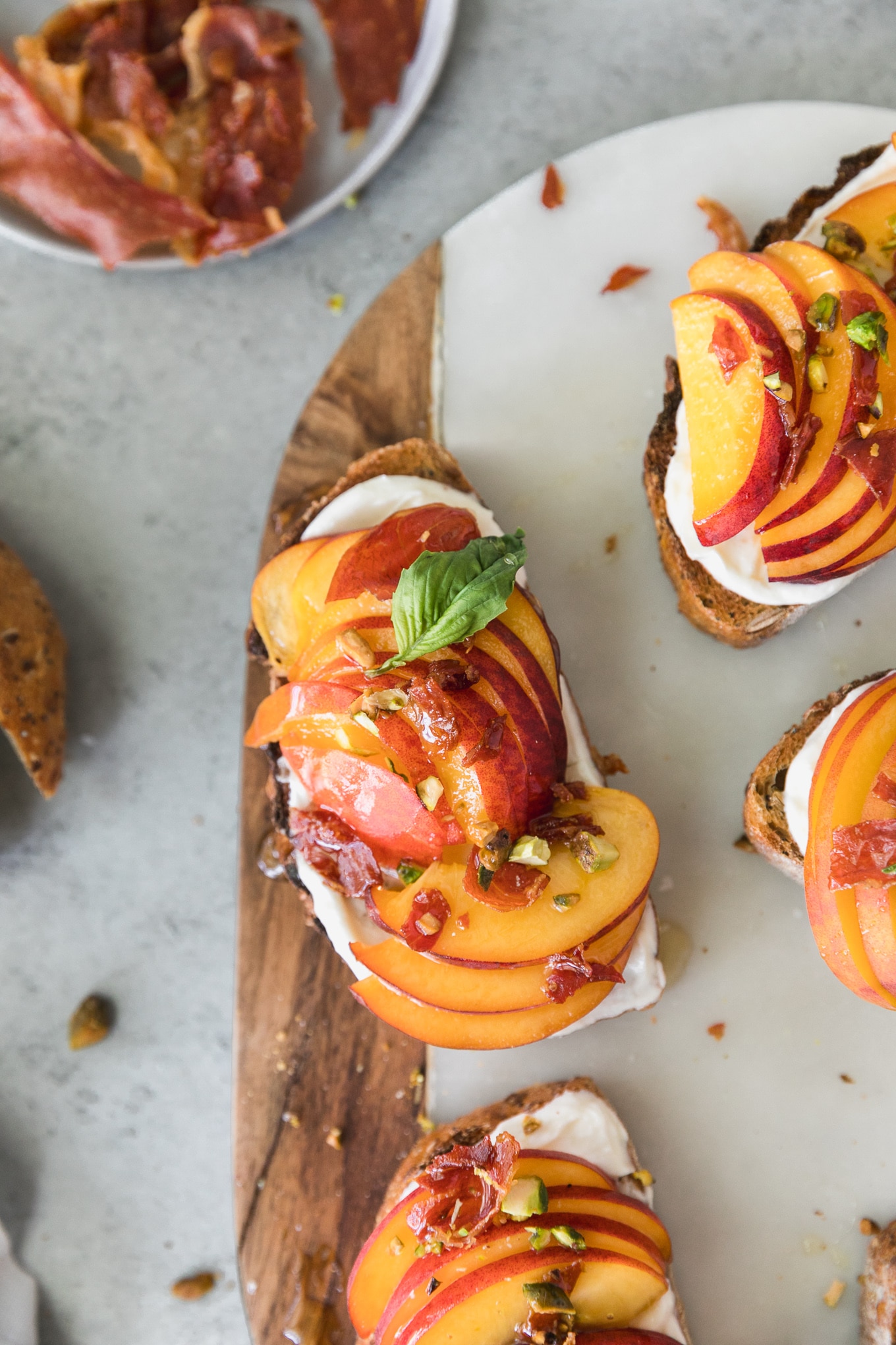 Overhead shot of a piece of toast topped with peaches, honey, basil, and chopped pistachios