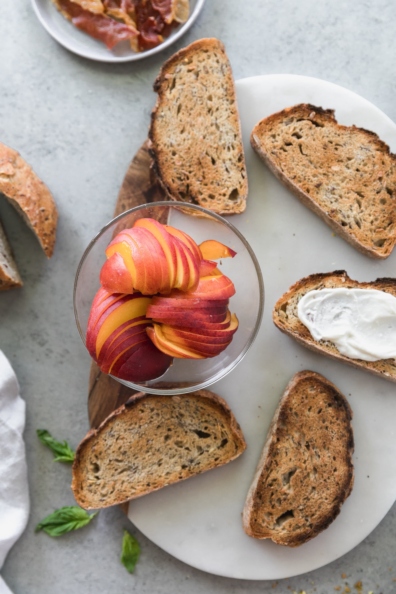 Overhead shot of a board topped with 5 slices of toast and a bowl of sliced peaches 