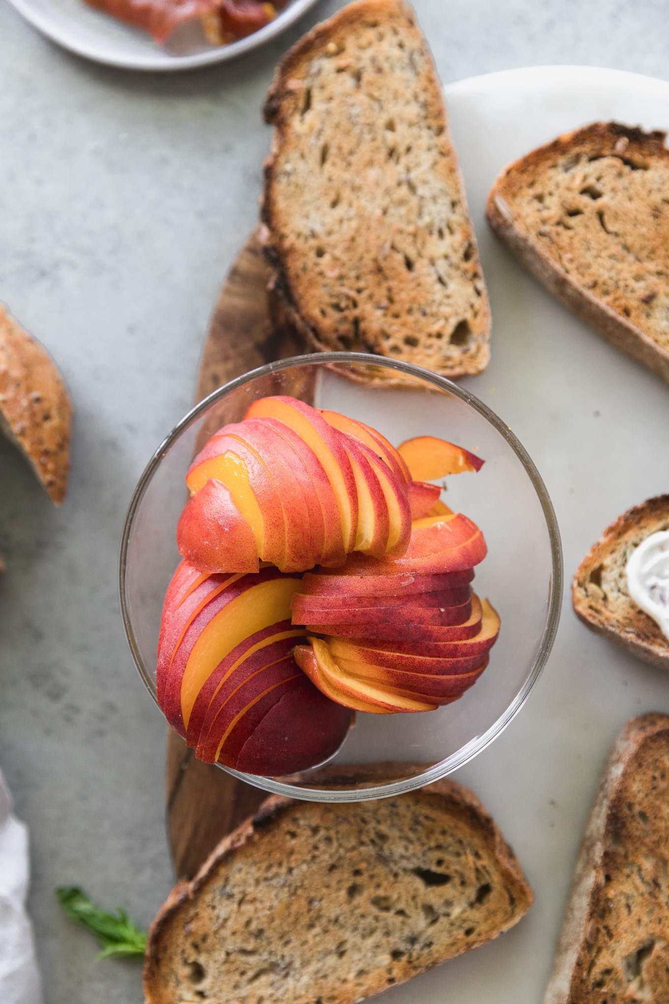 Overhead shot of a bowl of sliced peaches surrounded by pieces of toast