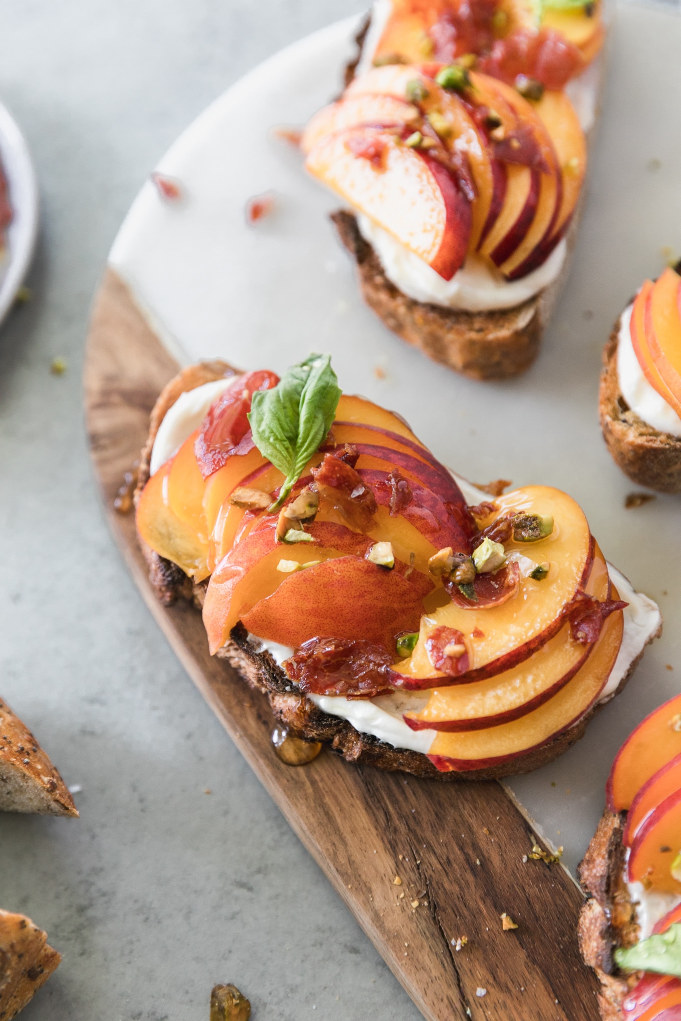 Close up shot of a piece of toast topped with ricotta, sliced peaches, chopped pistachios, basil, and honey