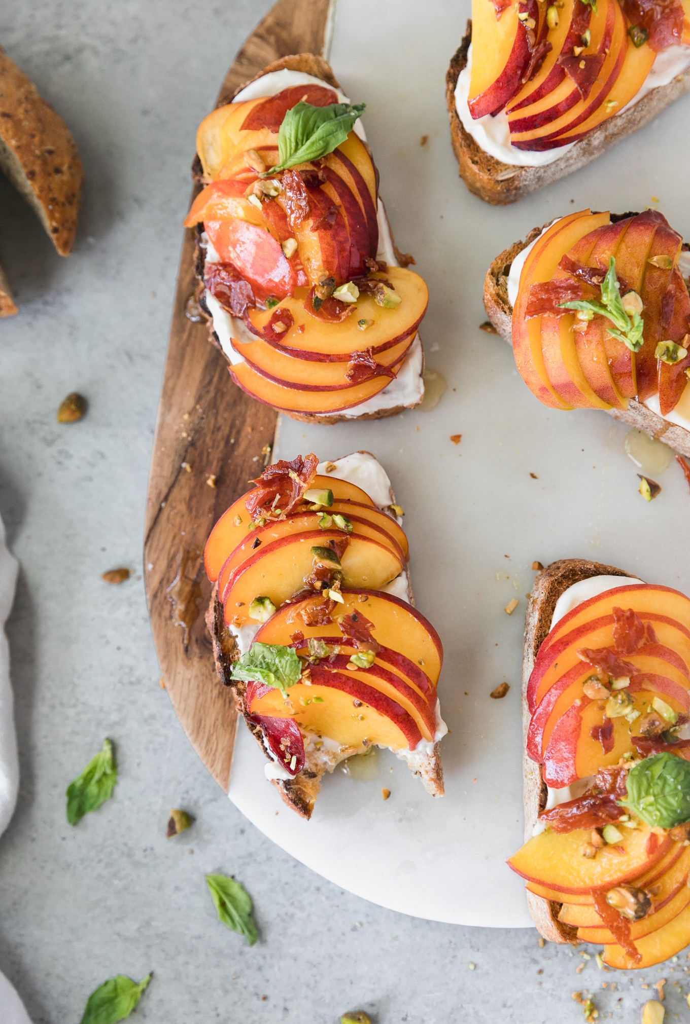 Overhead shot of a marble and wooden board topped with peach toasts, with a bite taken out of one of them