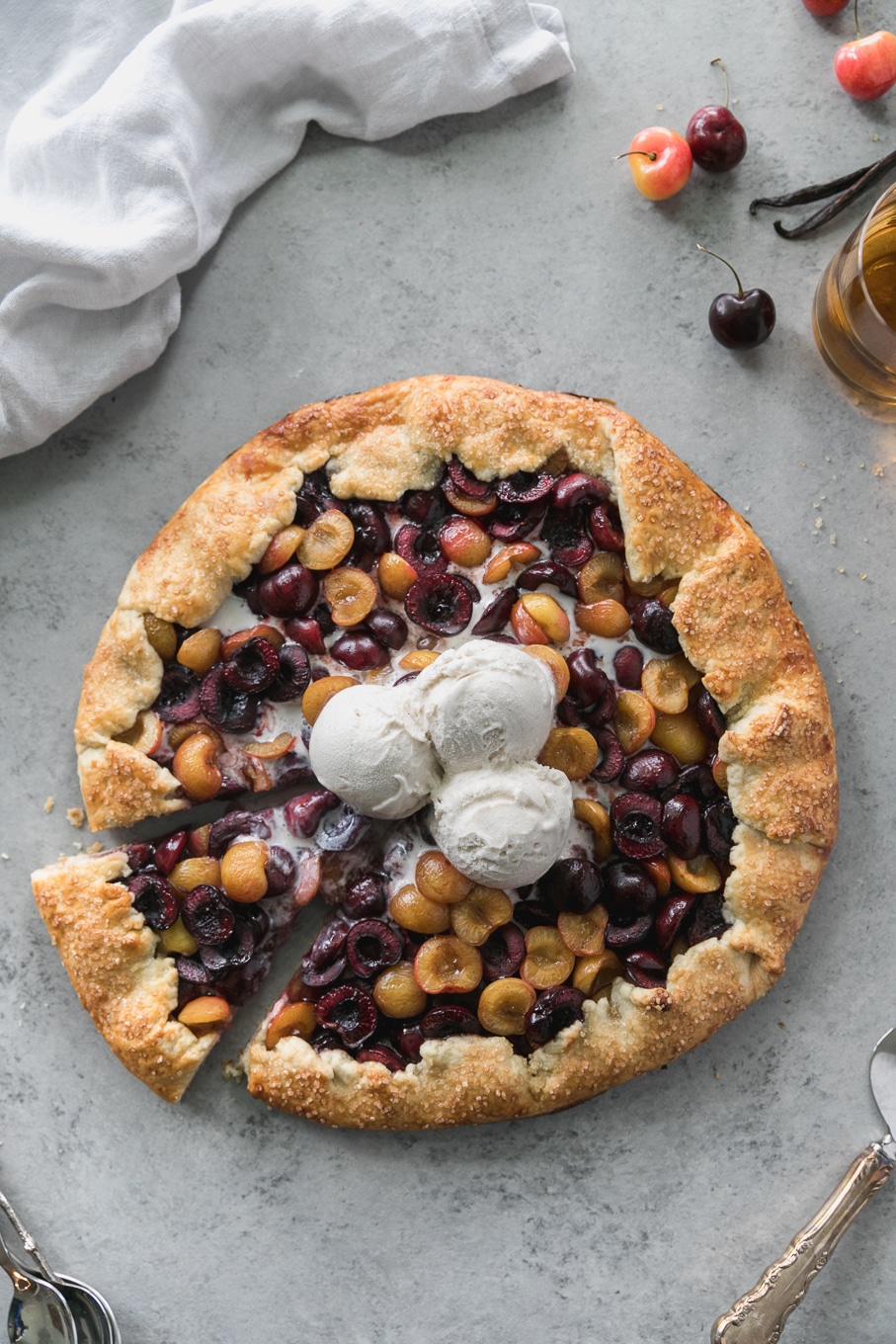 Overhead shot of a cherry galette with 3 scoops of ice cream on top with a slice being taken out