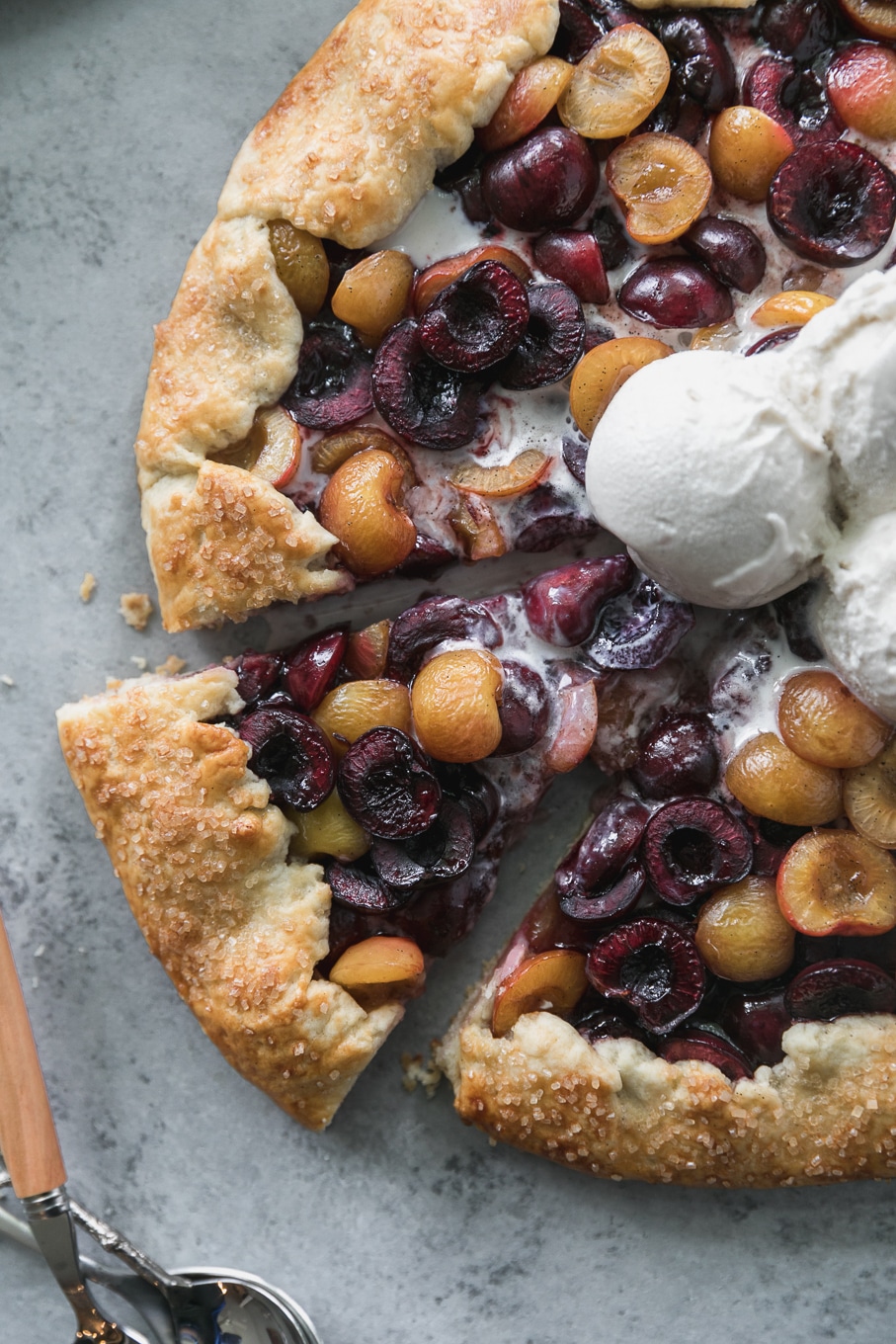 Overhead close up shot of a cherry galette with 3 scoops of ice cream on top with a slice being taken out