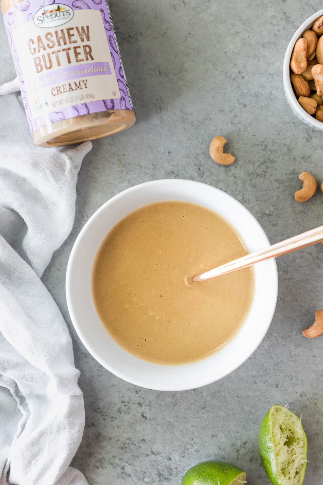 Overhead shot of a bowl of cashew dressing with a jar of cashew butter above it and roasted cashews scattered around