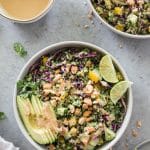Overhead shot of a salad with cashews, avocado, and lime wedges with a bowl of cashew dressing above it