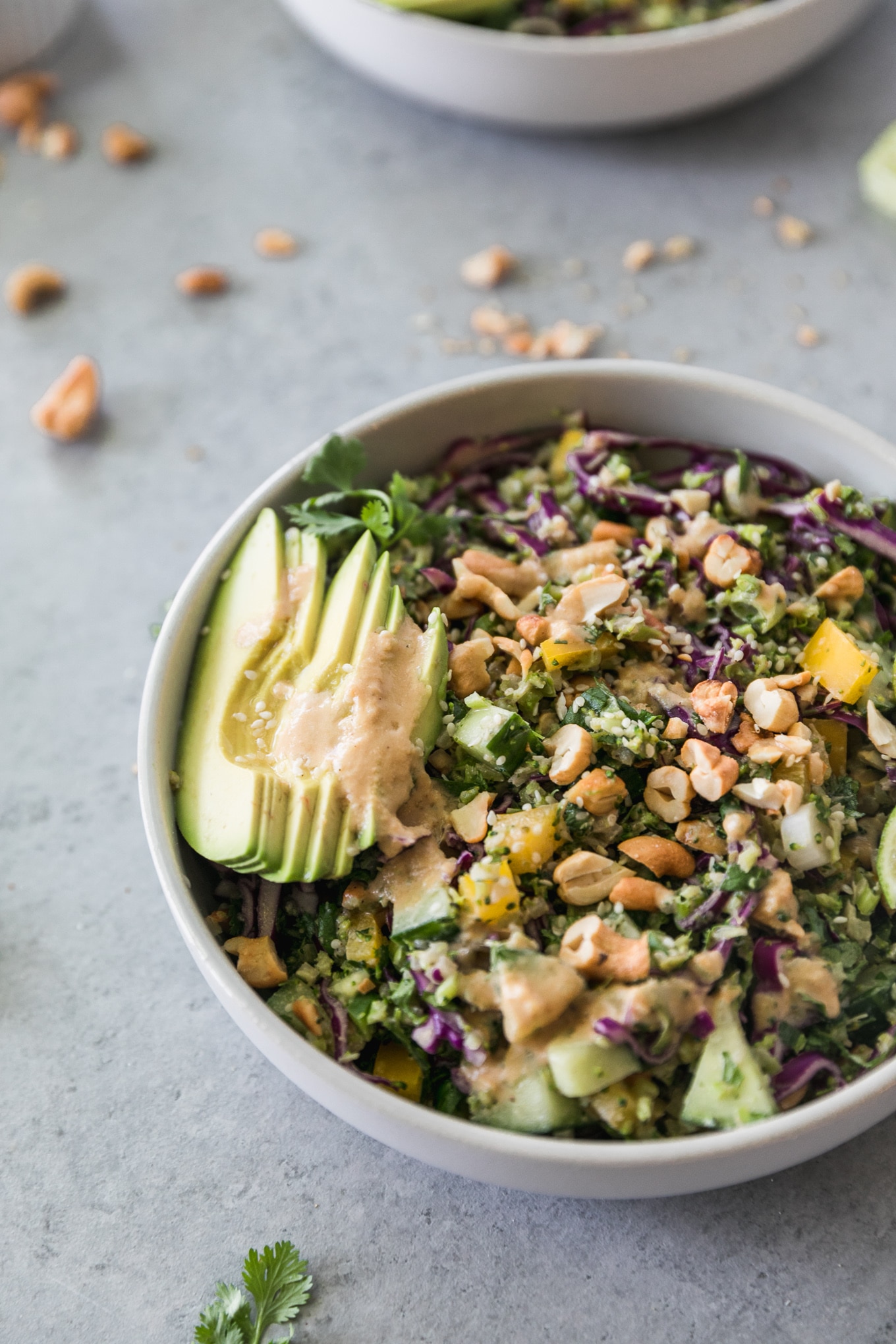 Close up shot of a crunchy vegetable salad with sliced avocado and cashews on top