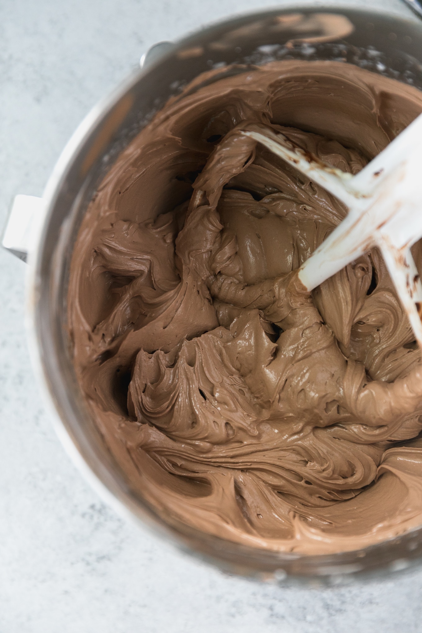 Overhead shot of a bowl filled with chocolate swiss meringue buttercream and a white mixing paddle in the bowl