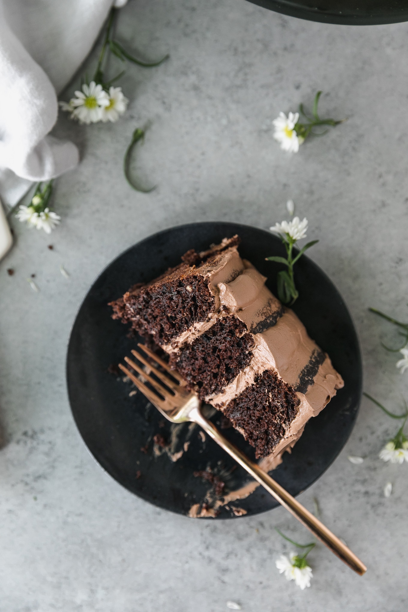 Overhead shot of a slice of chocolate cake with bites taken out of it with a gold fork resting on the black plate